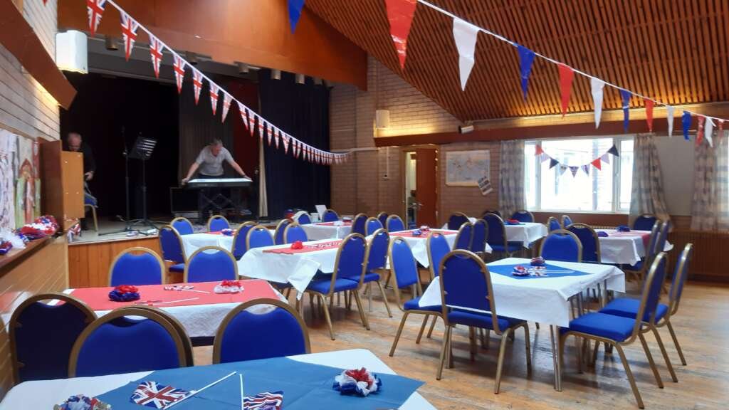 Event hall decorated with red, white and blue bunting, tables set for a party, and a musician at a keyboard on stage.